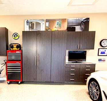 Garage storage cabinets, drawers, and TV. A red tool chest is nearby. A white sports car is partially visible.