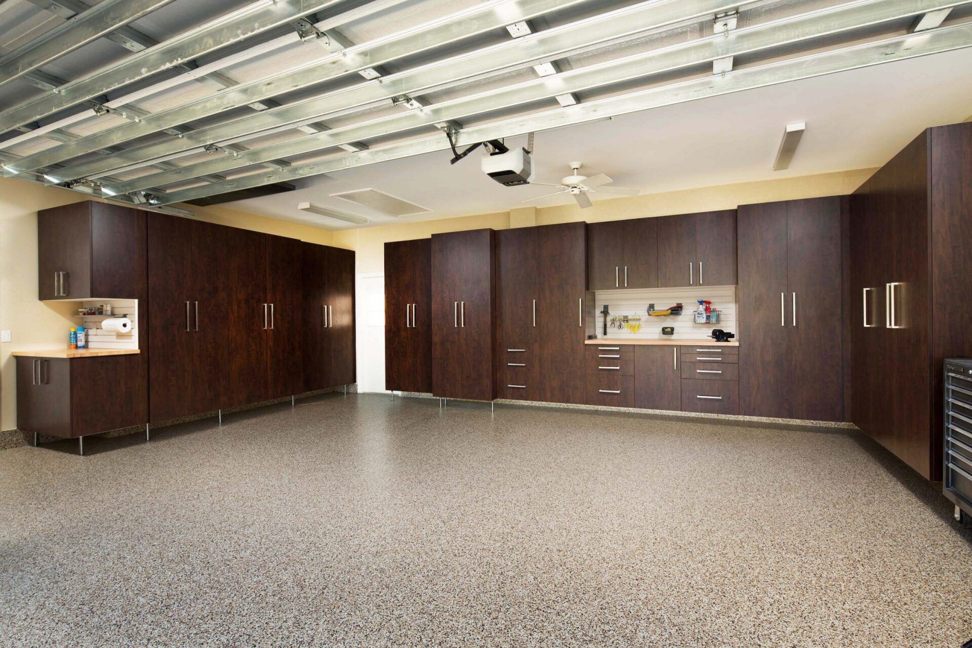 Dark wood cabinets line a garage with a speckled gray floor and exposed ceiling beams.