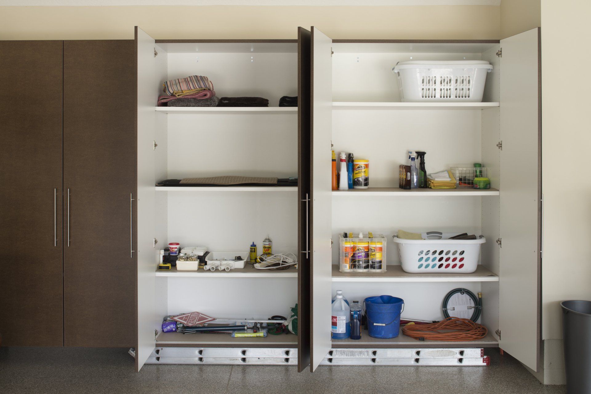 Brown and white cabinets with open doors reveal shelves holding various household items in a garage.