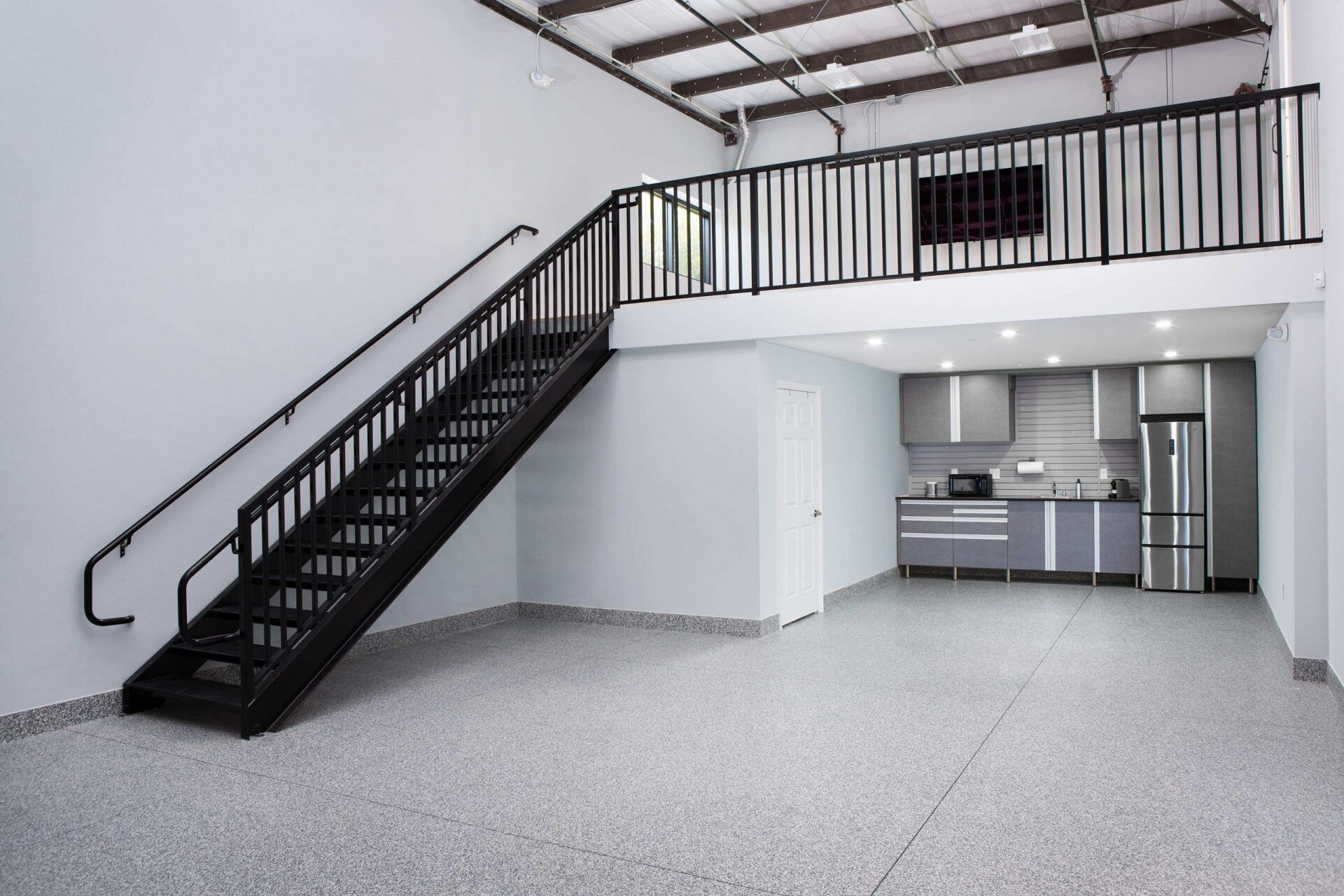 Empty interior with a metal staircase leading to a loft. Includes a kitchen and gray speckled flooring.