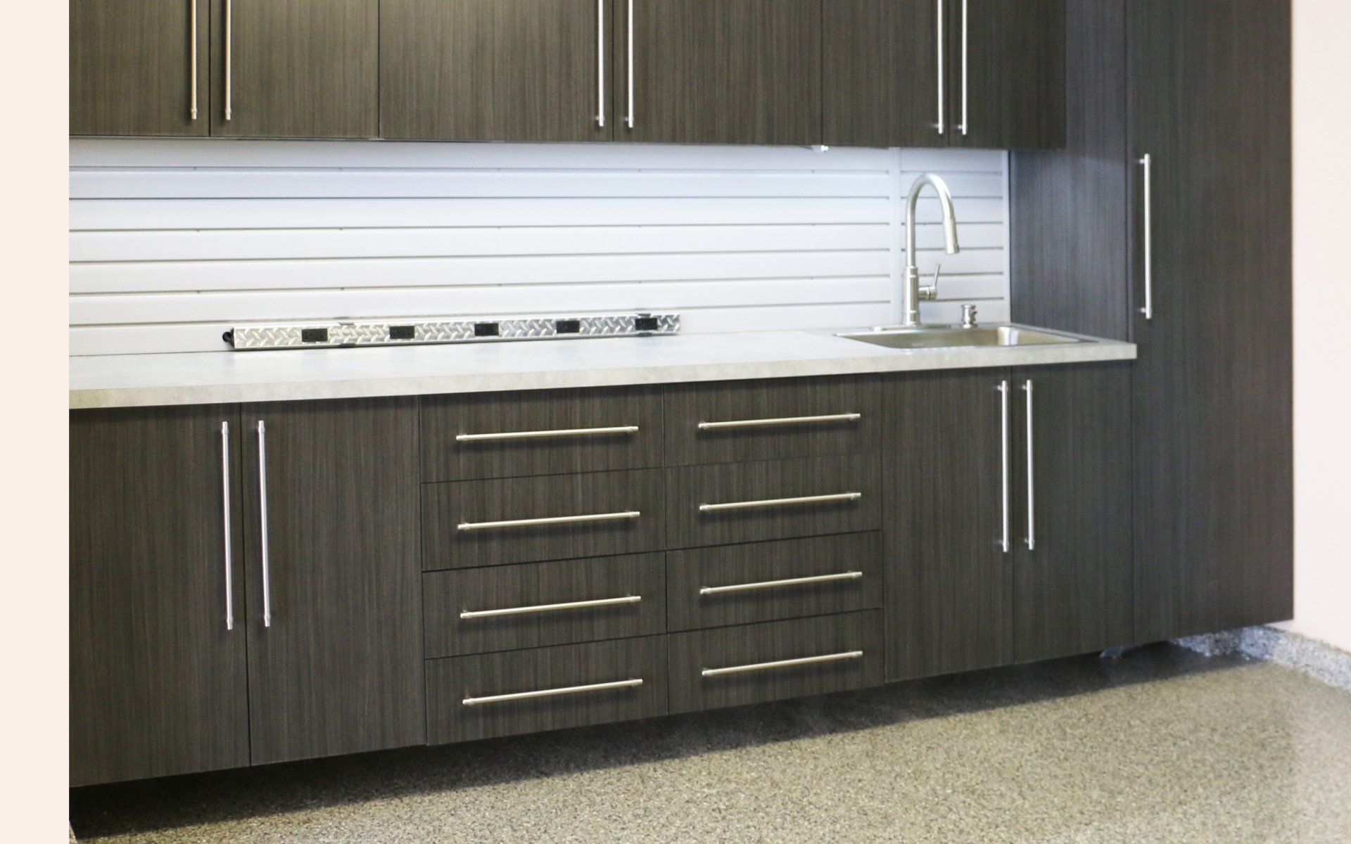 Dark gray cabinetry with stainless steel handles, countertop, and sink in a garage setting.