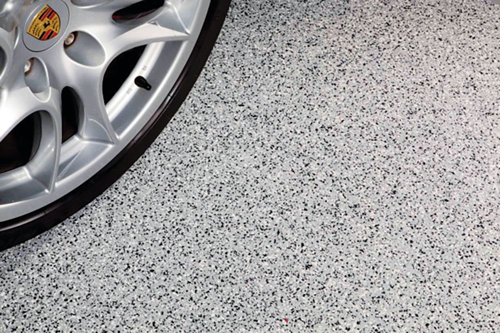 Silver Porsche wheel on a speckled gray garage floor.