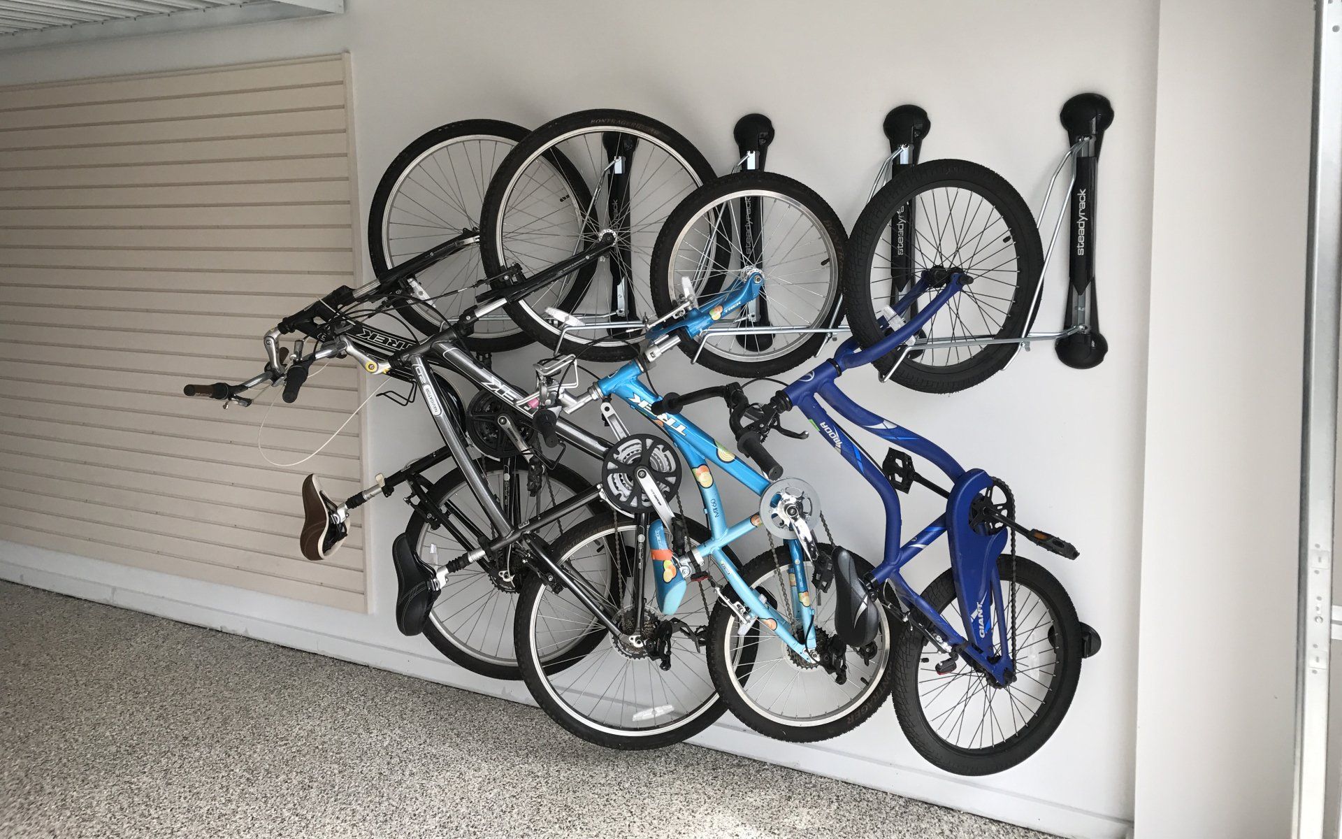 Bikes hanging on a wall-mounted rack in a garage. Various bike styles and colors are visible.