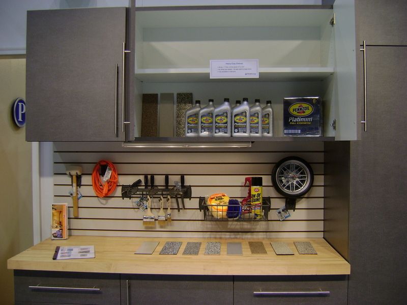 Garage workbench with overhead storage, containing tools, supplies, and open cabinet showing oil bottles and shelving.