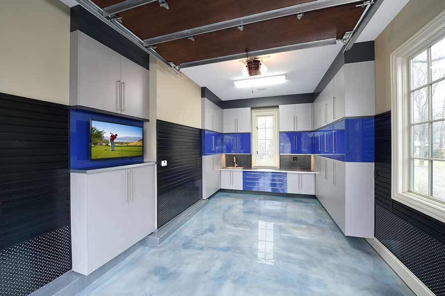 Modern garage interior with blue and white cabinets, TV, and epoxy floor.