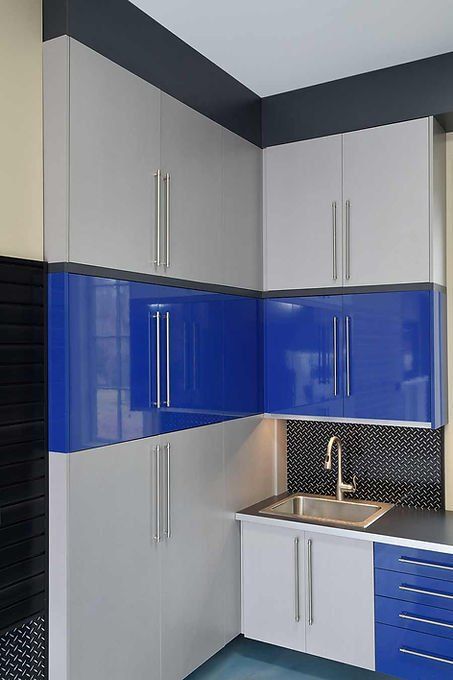 Corner kitchen cabinets in gray and blue, with a stainless steel sink and black countertop.