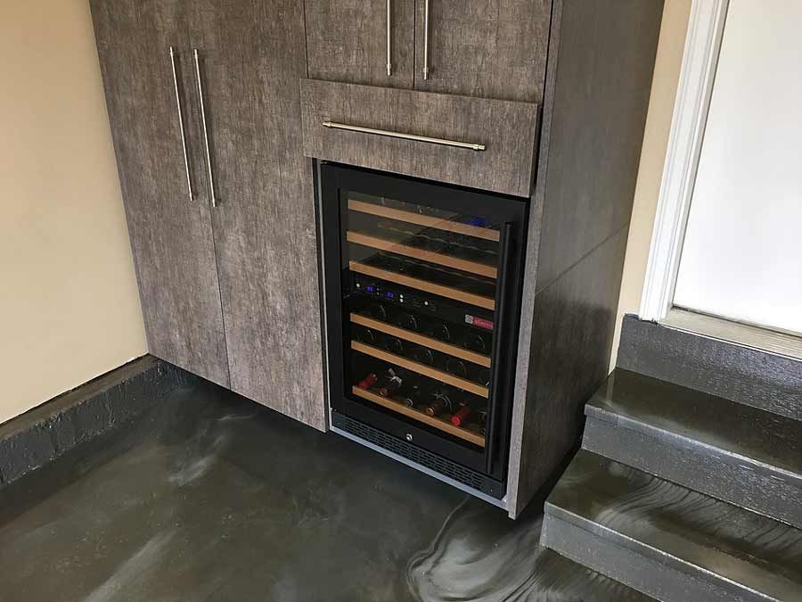 Built-in wine cooler in gray cabinet; garage setting with gray floor and stairs.