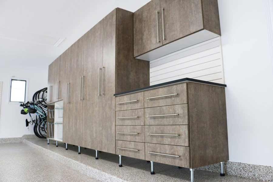Garage storage cabinets in a light wood grain finish, against a white wall and speckled floor.