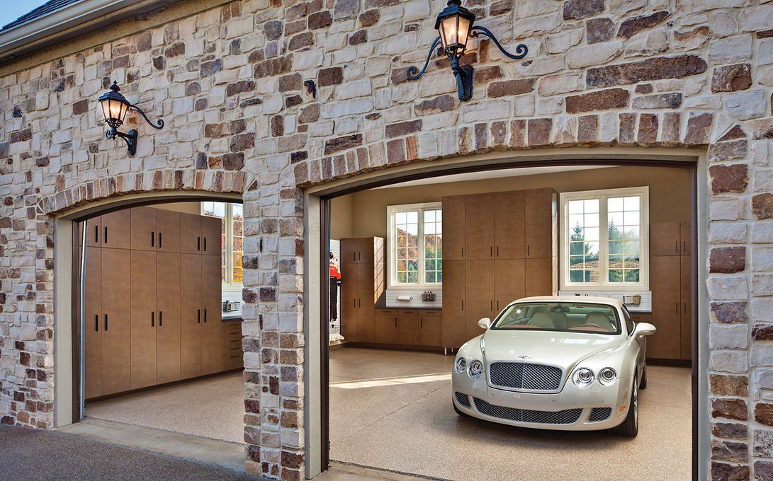Stone exterior garage with two bays, a silver car parked in one, and storage cabinets.