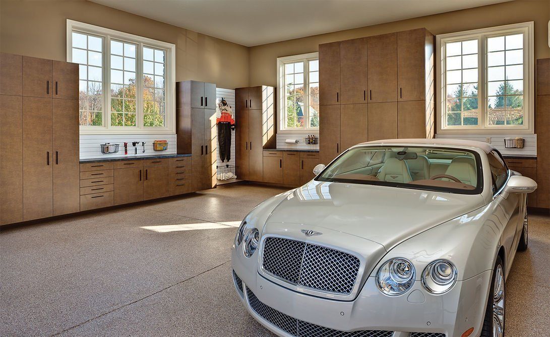 White Bentley in a well-lit garage with brown storage cabinets and windows.