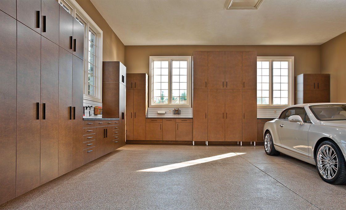 Spacious garage with wood cabinets, two windows, and a silver car parked on speckled floor.
