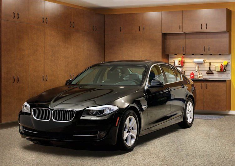 Black car parked in a garage with wood cabinets and a gray floor.