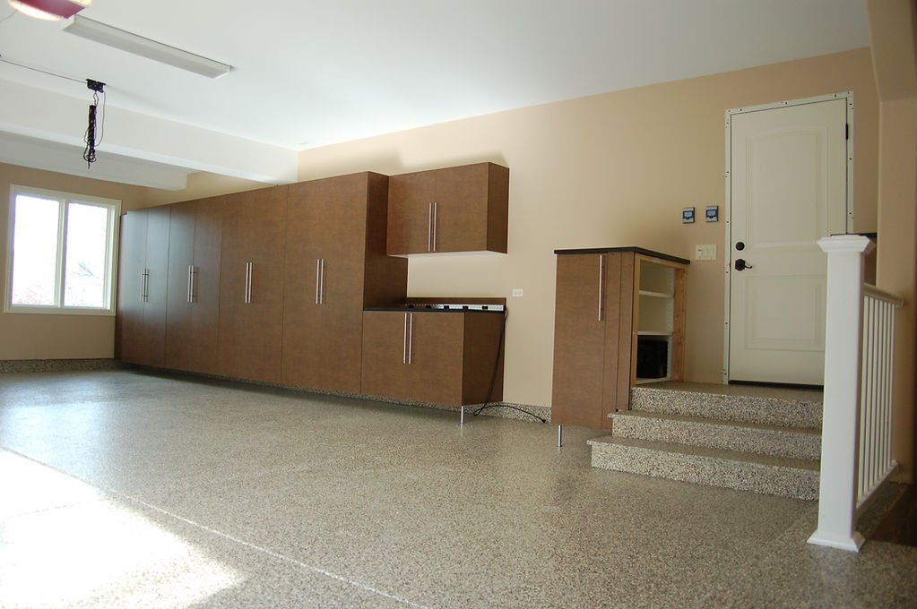 Empty garage with brown cabinets, a white door, and speckled floor.