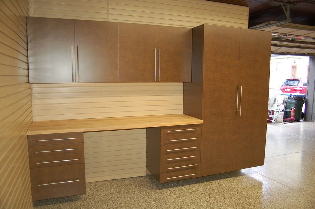 Brown cabinets, desk, and storage in a garage setting with open door and vehicle in the distance.