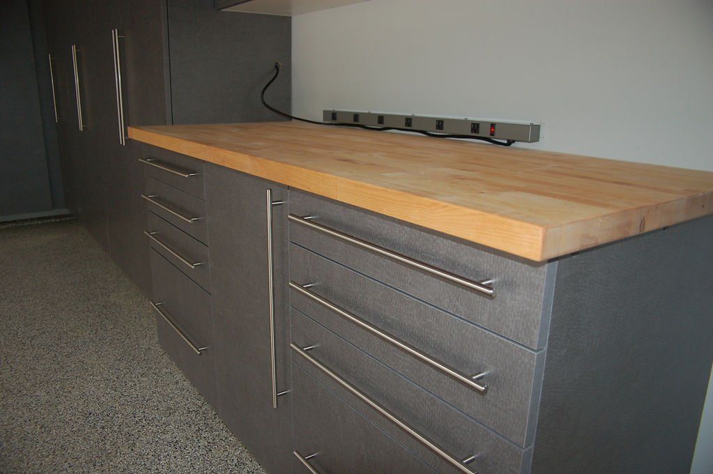 Gray cabinets with stainless steel handles and wood countertop; power strip on the wall.