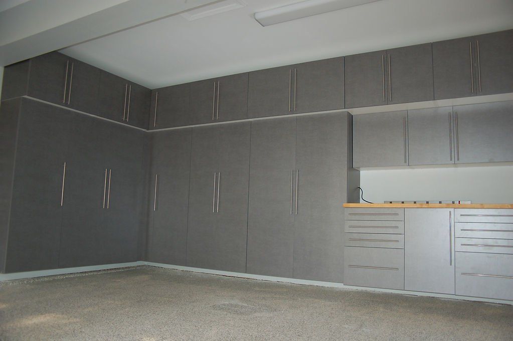 Gray garage cabinets, including upper and lower cabinets, line the walls of a garage with a tan floor.