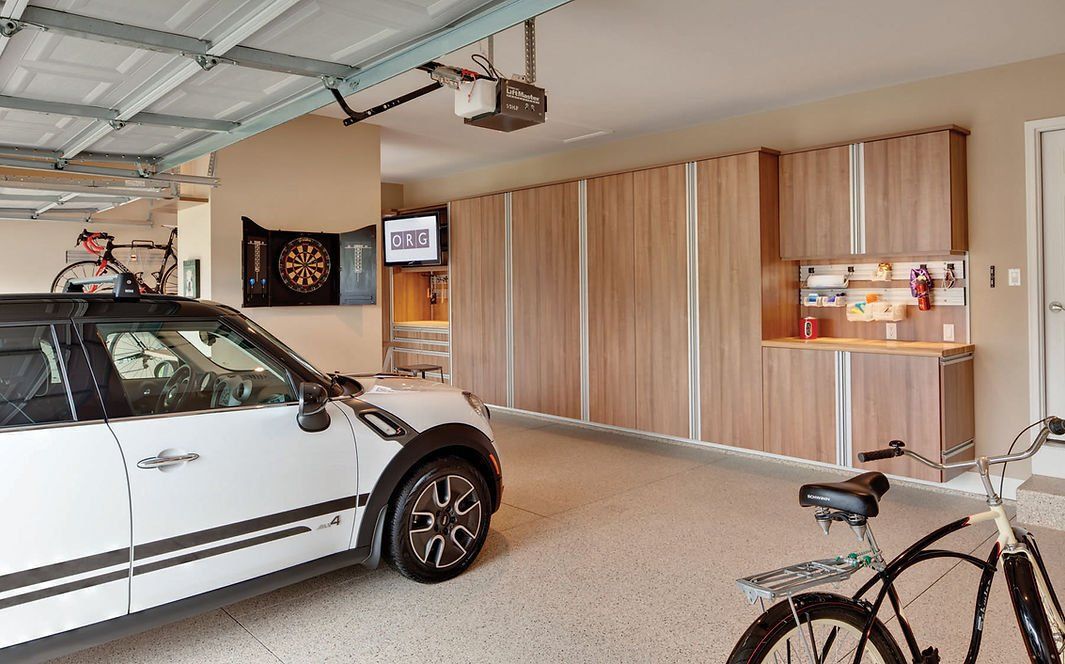 White car parked in a modern garage with wooden cabinets, a bicycle, and a dartboard.