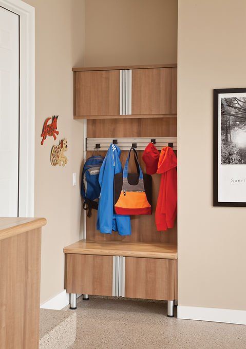 Entryway storage unit with coats, bags, and bench. Brown cabinets, tan walls, and a framed print.