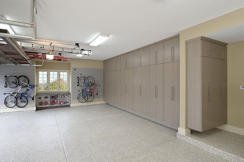 Spacious garage with light grey cabinets lining one wall, speckled flooring, and bikes on the other.