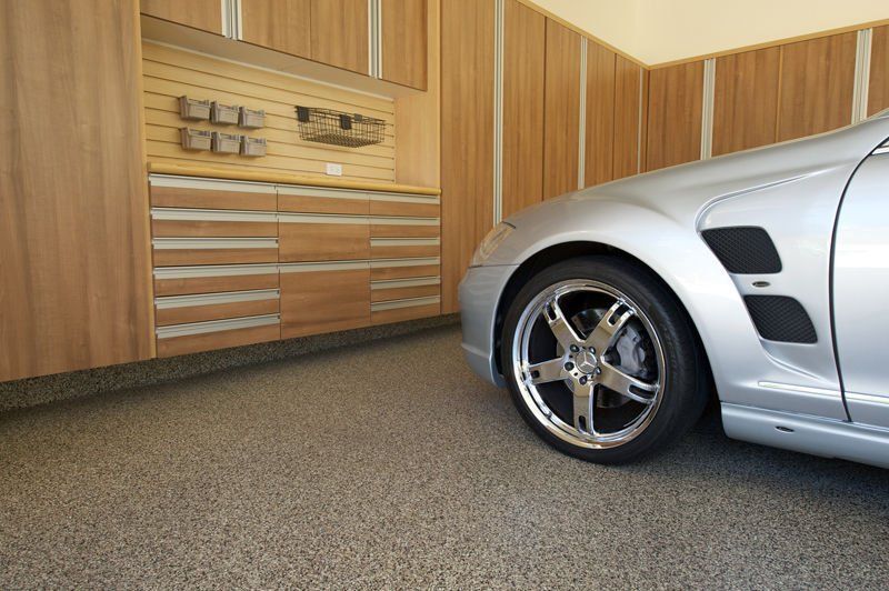 Silver car parked in a garage with wood cabinets and a speckled floor.