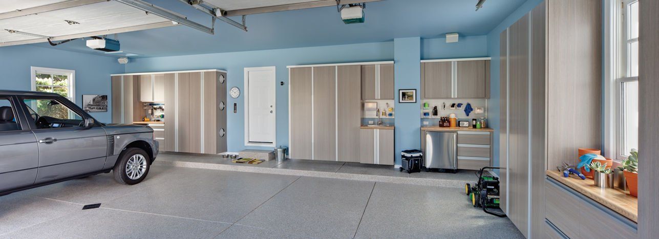 A clean garage interior with a gray SUV parked on the left. Blue walls and cabinets.