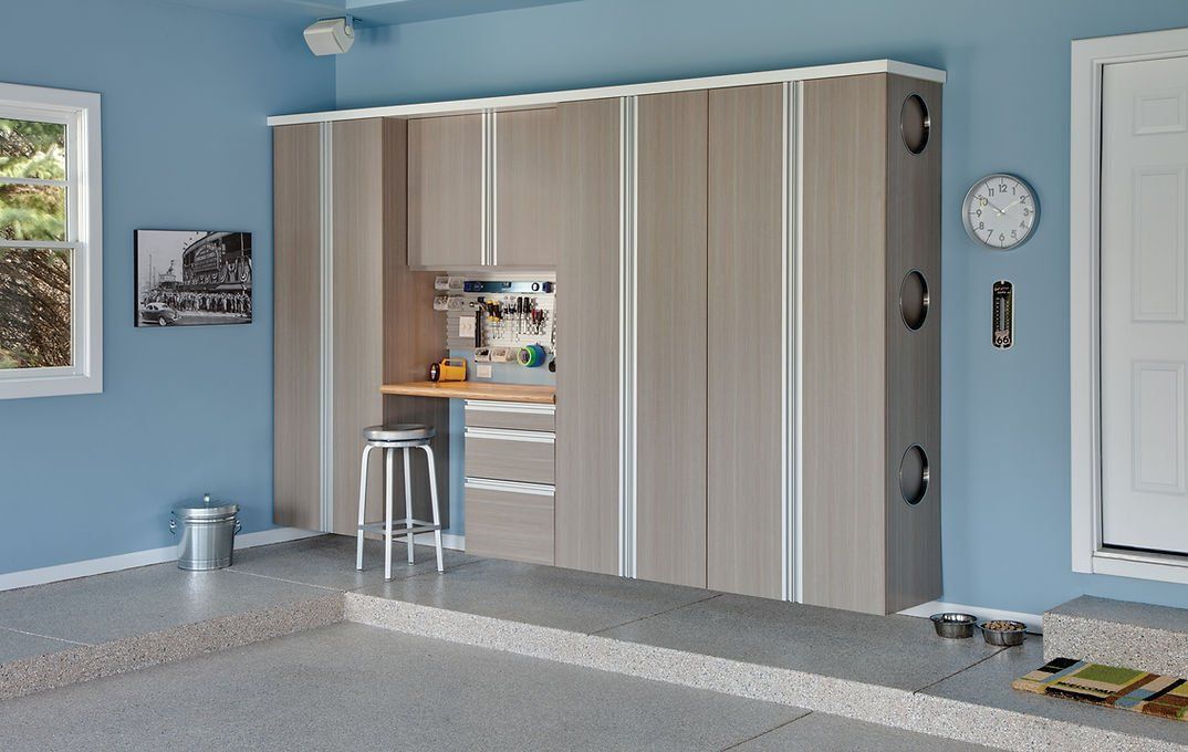 Garage with built-in tan storage cabinets, workbench, and blue walls. Features a window, door, and a stool.