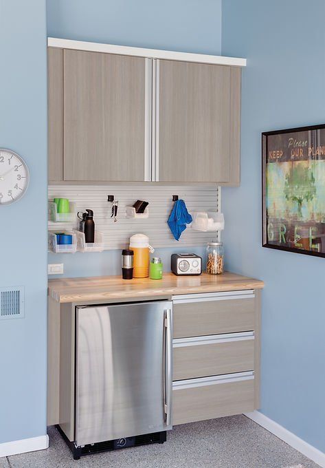 Garage storage space with cabinets, countertop, refrigerator, and pegboard organizer. Light blue walls.