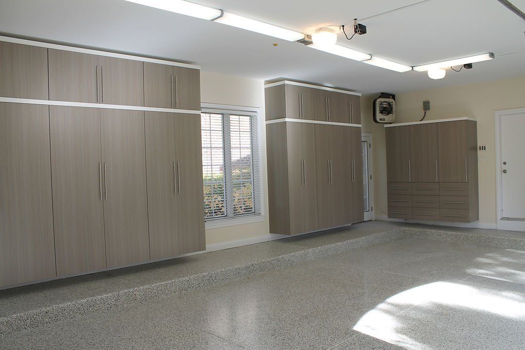 Garage with gray cabinets and a gray speckled floor. Fluorescent lights and a window are visible.