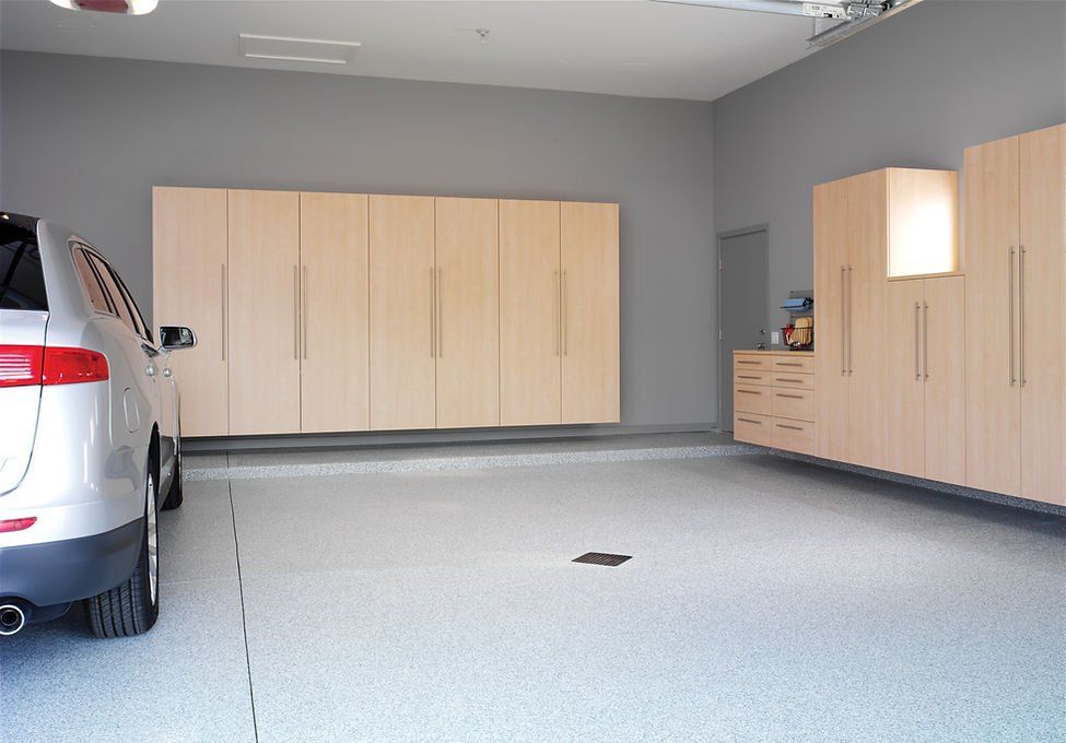 Spacious garage with light-colored cabinets, a car parked inside, and a light speckled floor.