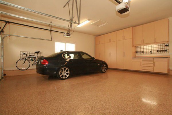 A spacious, clean garage with a black car, cabinets, and a bicycle. The floor is speckled.