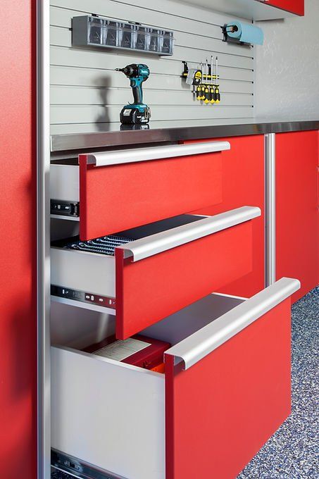 Red cabinet with three open drawers, silver handles, tools visible on wall above.