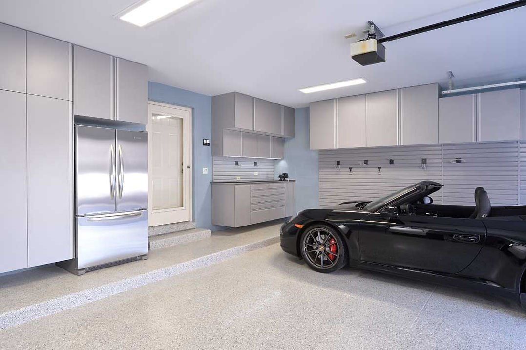 Modern garage with a black sports car, stainless steel refrigerator, and gray cabinetry.