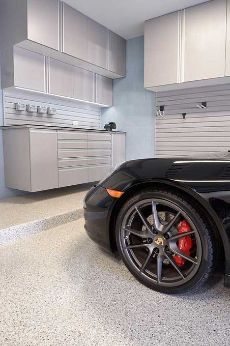 Black sports car in a modern garage with custom storage cabinets and a speckled floor.