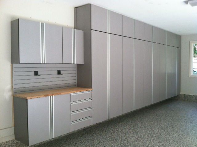 Gray garage cabinets with a wood countertop and pegboard, mounted on a wall with a speckled floor.