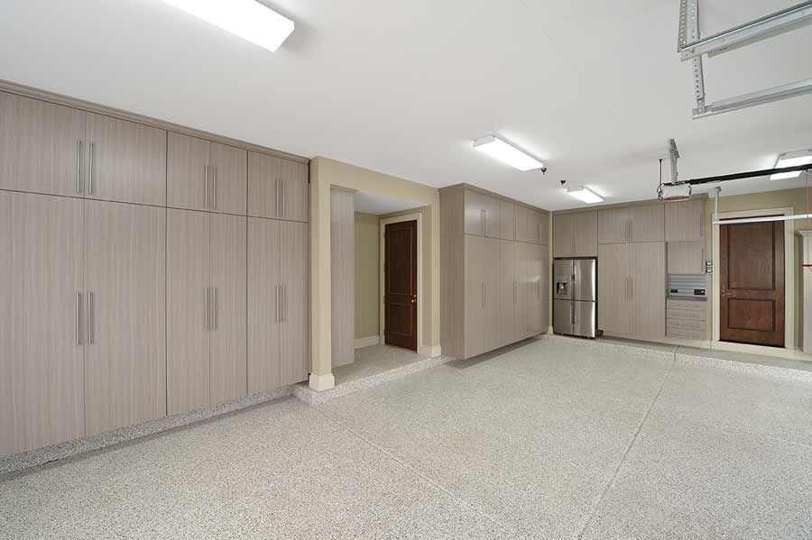 Garage with light-colored cabinets, a stainless steel refrigerator, and a speckled floor.