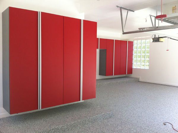 Red garage cabinets against white walls, set in a garage with speckled flooring.