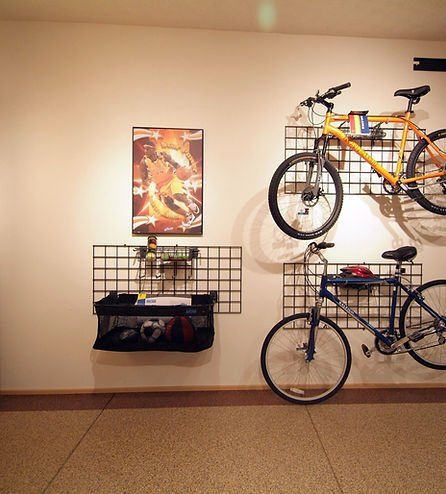 Garage wall with mounted storage: two bikes, grid shelves with sports equipment, and a poster.