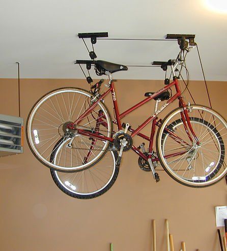 Red bicycle suspended from ceiling storage system in garage.