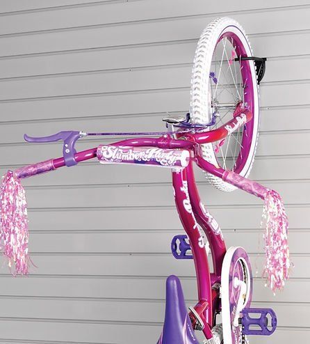 Pink children's bicycle hanging from a black wall-mounted bike rack on a gray wall.