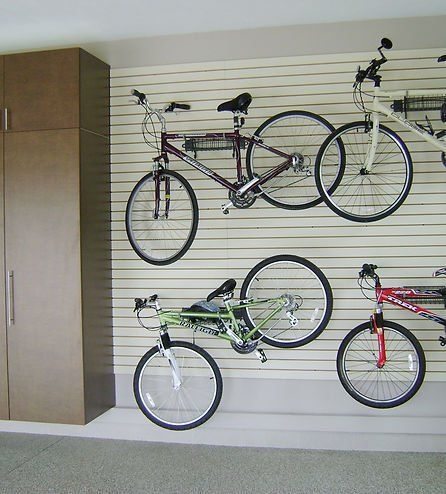 Bicycles mounted on a slotted wall, next to a tall brown cabinet, in a garage.
