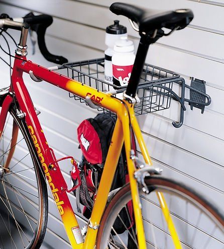 Red and yellow Cannondale bike mounted on garage wall with a basket and water bottles.