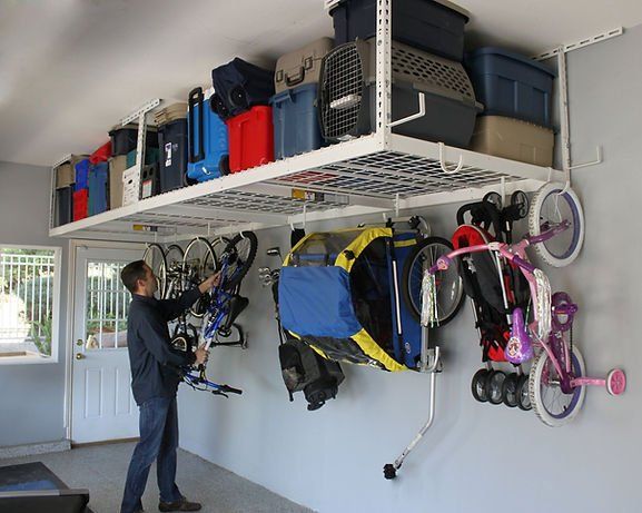 Man storing a bicycle in a garage with overhead storage and wall-mounted bike racks.