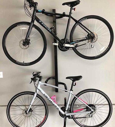 Two bicycles mounted on a vertical bike rack on a beige wall. One is black, the other is white.
