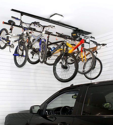 Bicycles hanging from a ceiling-mounted rack in a garage, next to a black car.