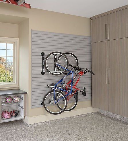 Garage wall with slat system holding two bicycles. Gray, tan, and beige color scheme. Cabinets and a window are also visible.