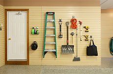 Garage wall with tools hanging. Door at left, ladder, shovel, broom, and other tools.