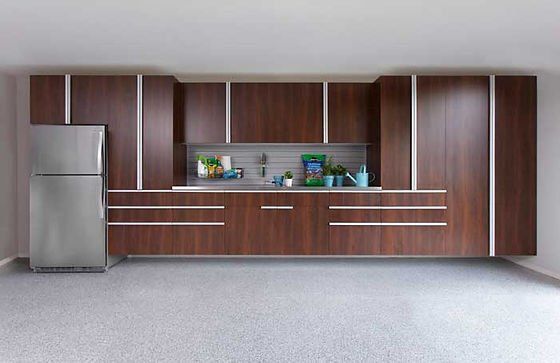 Kitchen cabinets and stainless steel refrigerator on a gray floor. Brown cabinets with silver trim.