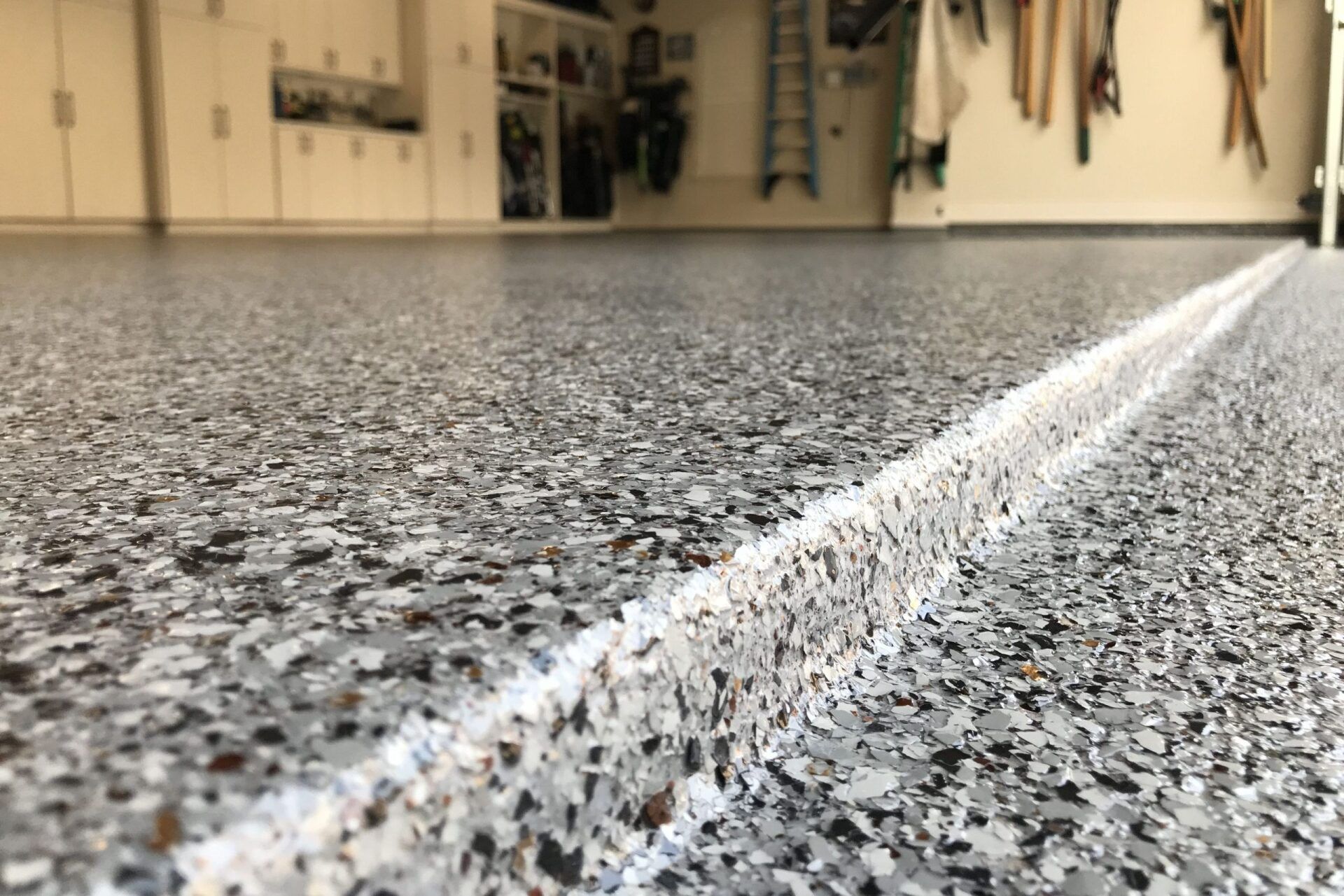 Close-up of a garage floor with a gray and white speckled epoxy coating, a white seam runs along the center.