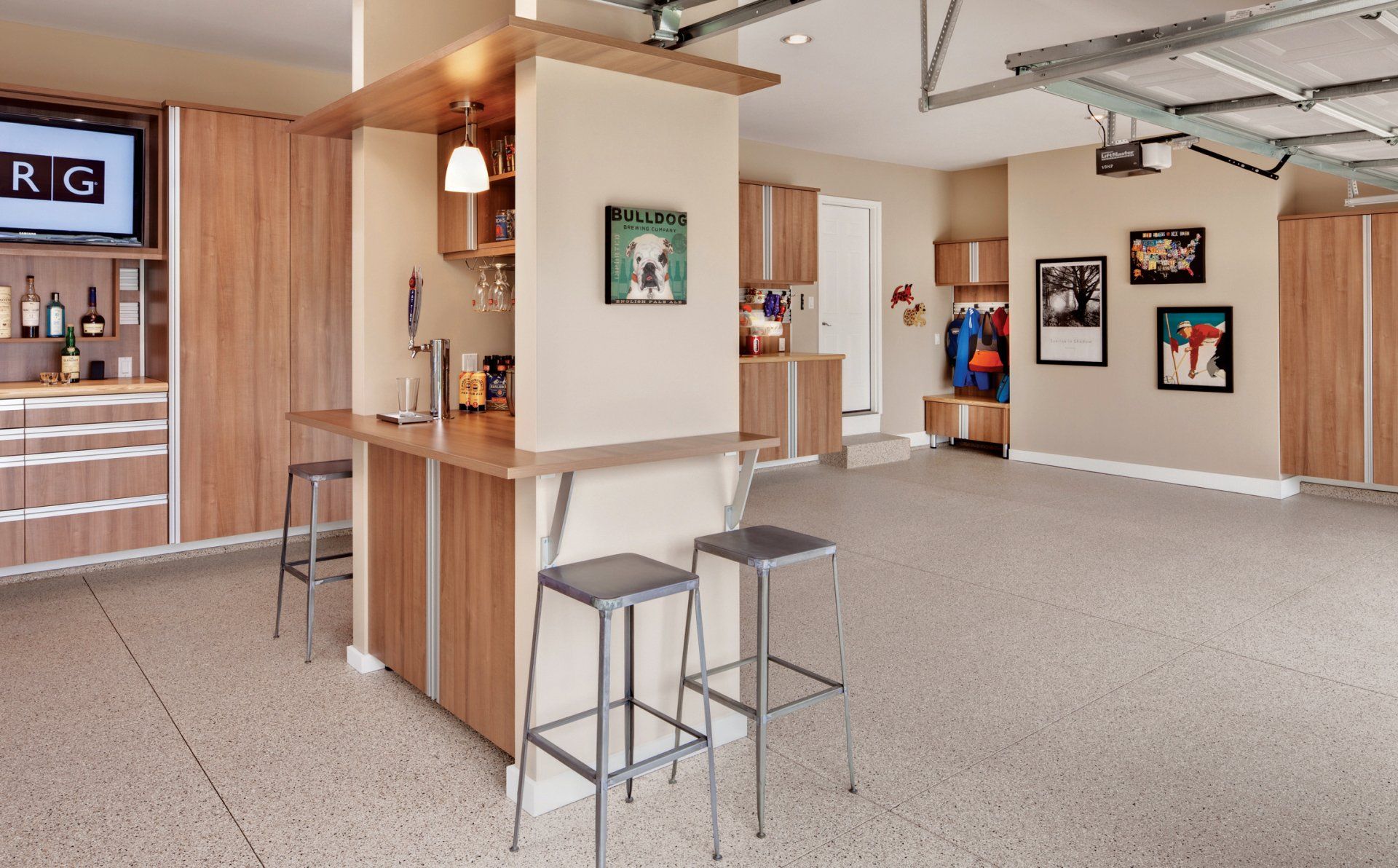 Garage interior with built-in bar, storage cabinets, and bar stools. Epoxy floor and overhead garage door are visible.