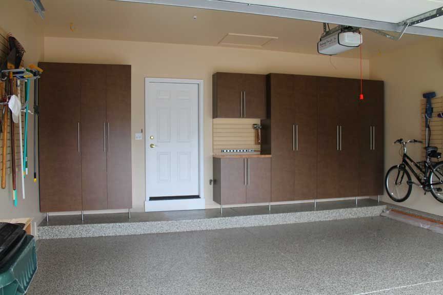 Garage interior with brown storage cabinets, white door, bicycle, and speckled floor.